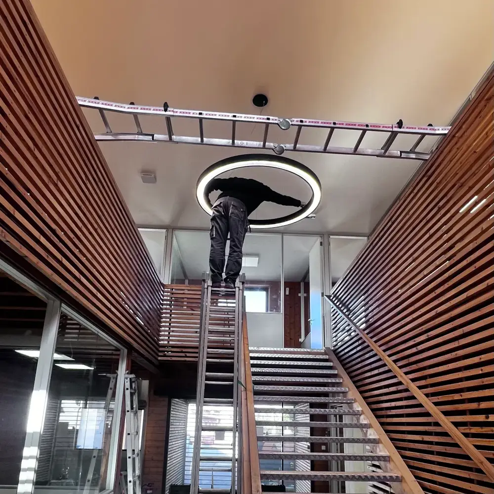 Pose d’un luminaire LED circulaire en hauteur dans un bâtiment professionnel par Eric Issartier